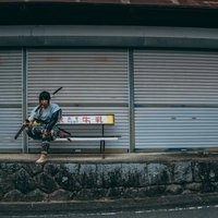 シャッター前のベンチに腰掛ける侍姿の男性の写真