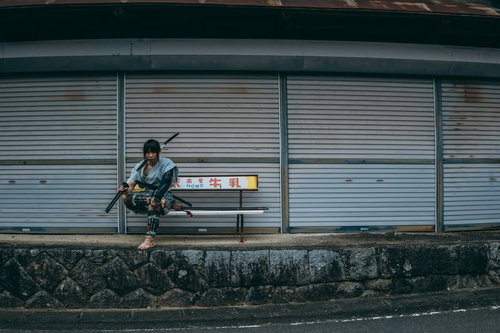 シャッター前のベンチに腰掛ける侍姿の男性