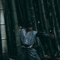薄暗い竹林の中から大弓を構える野盗の男性の写真