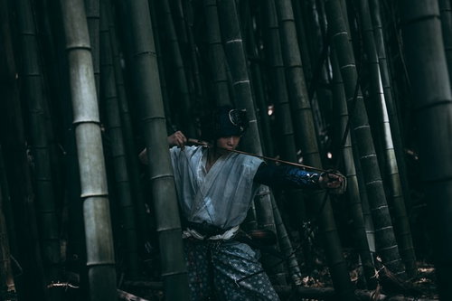 薄暗い竹林の中から大弓を構える野盗の男性