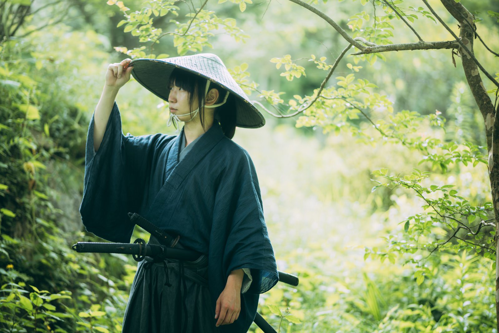新緑の森で編笠を被り黒い着物姿で刀を帯びた侍の男性［モデル：まーこ］
