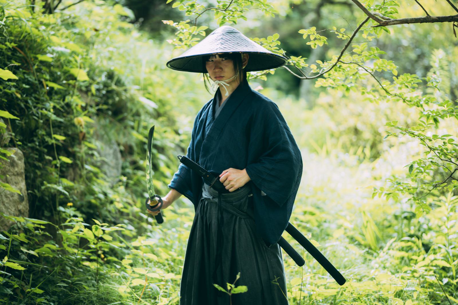 笠をかぶり藍色の着物に黒い袴姿で刀を構える侍の男性［モデル：まーこ］