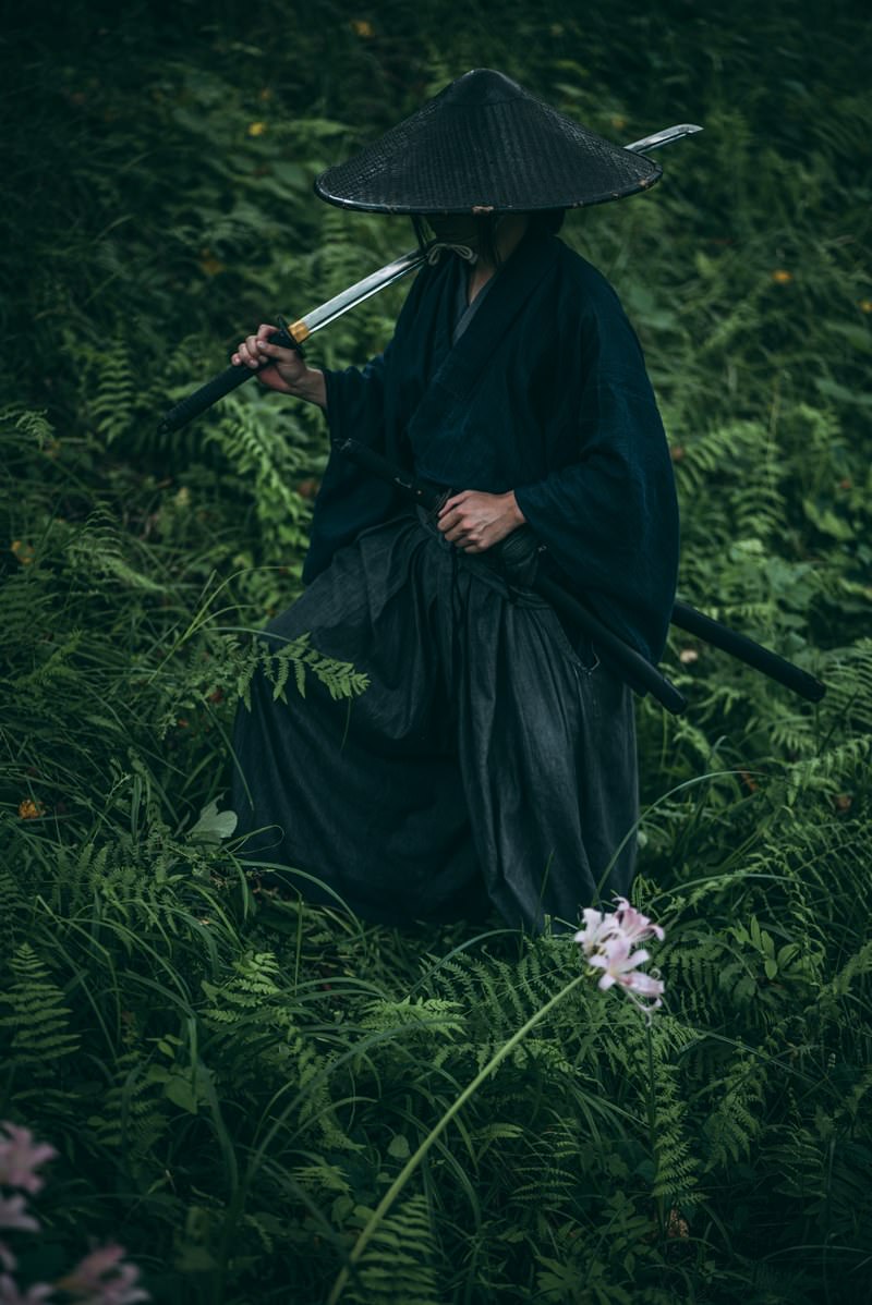 緑の草原で日本刀を構える網代笠を被った侍の男性［モデル：まーこ］