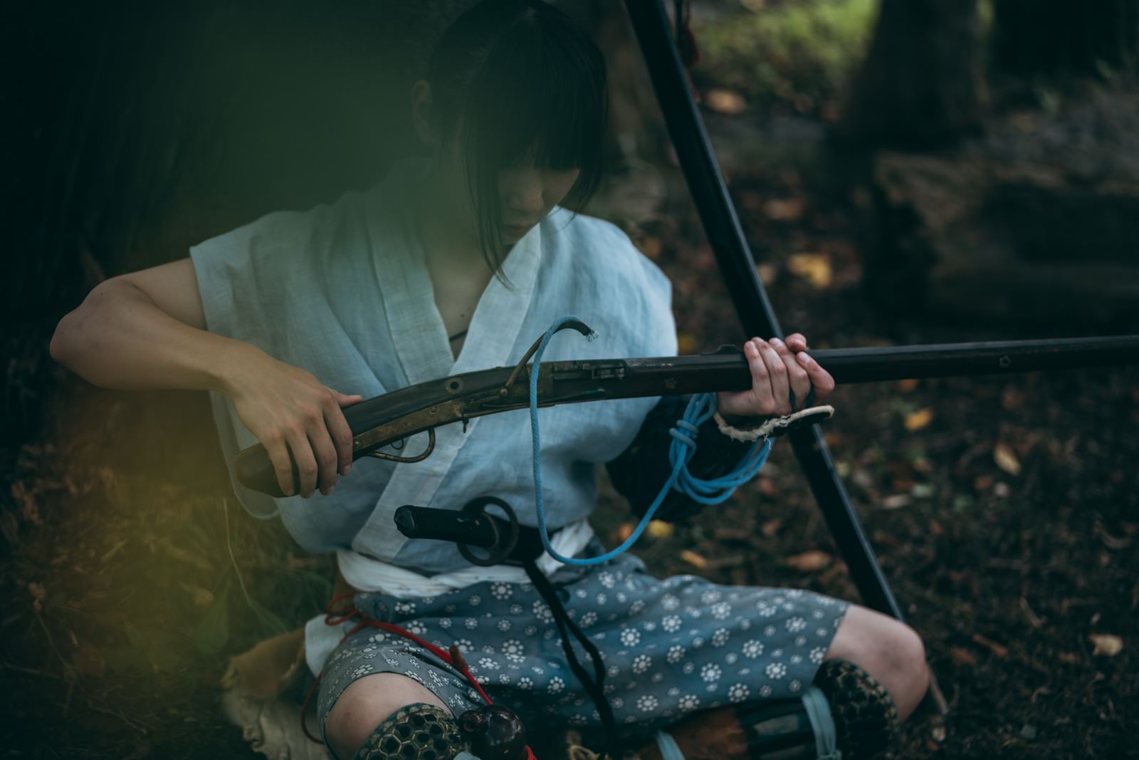 地面に座り込んで火縄銃の手入れをする半着姿の野盗男性［モデル：まーこ］