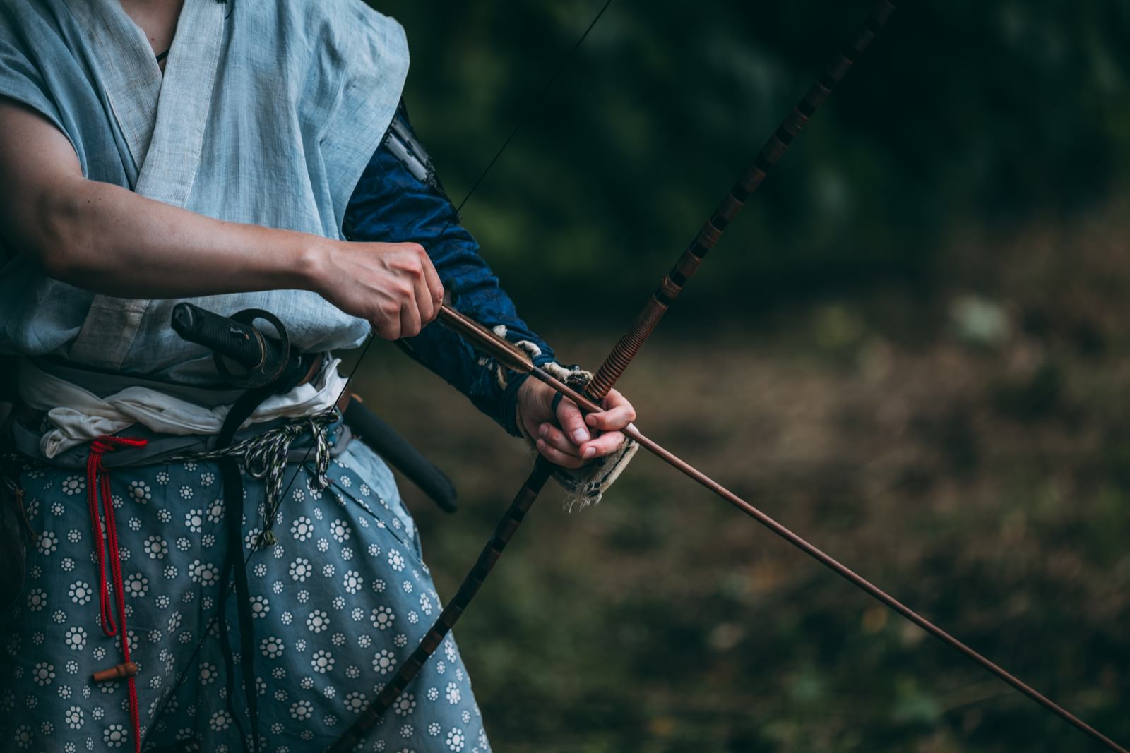 和装の男性が大弓を引いて狙いを定めている手元のクローズアップ［モデル：まーこ］