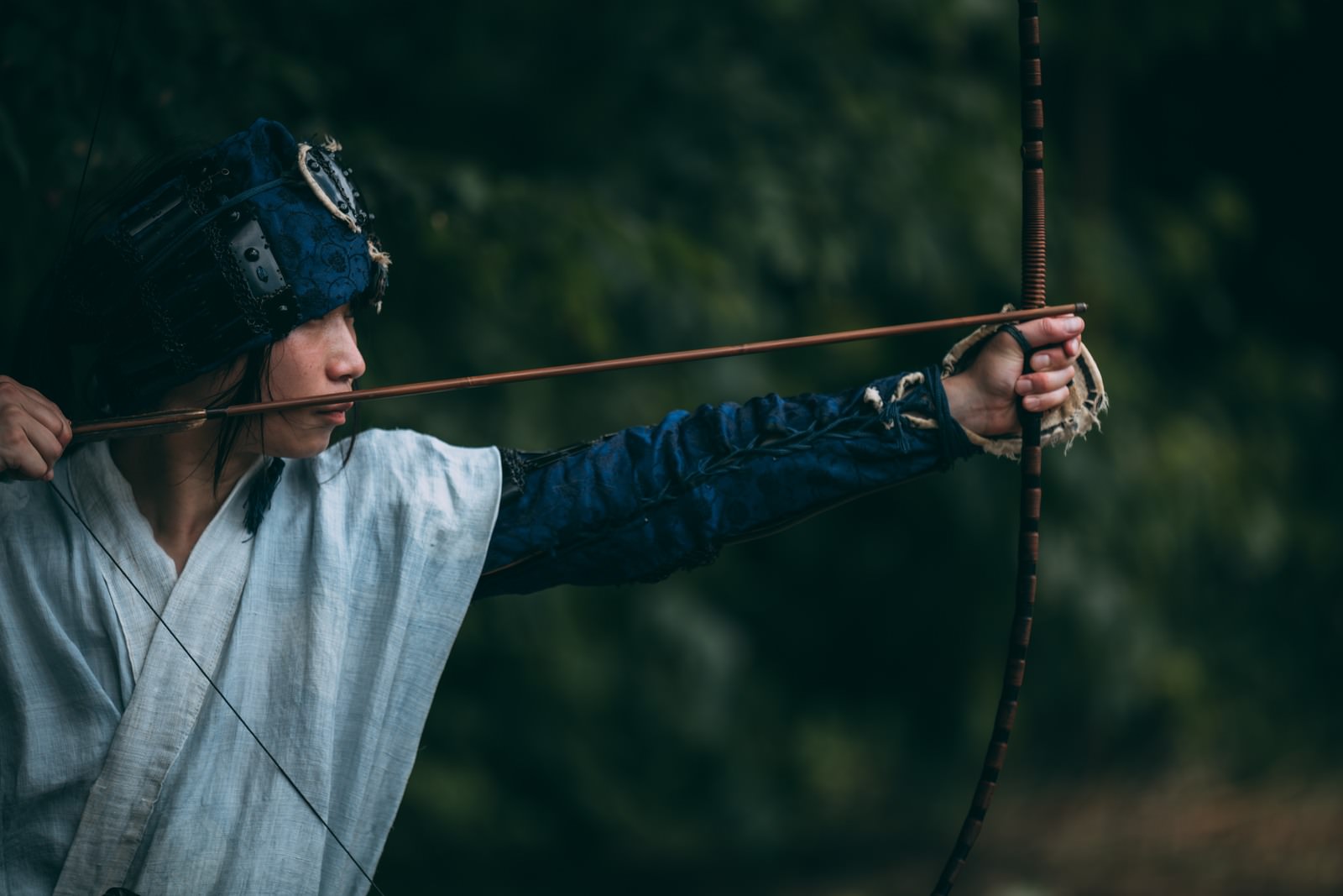 白い着物を着た男性が弓を構えて狙いを定めている［モデル：まーこ］