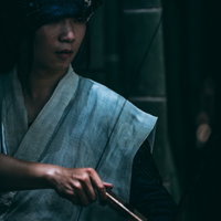 伏し目がちに大弓を引く野盗男性、時代劇キャラクターの写真