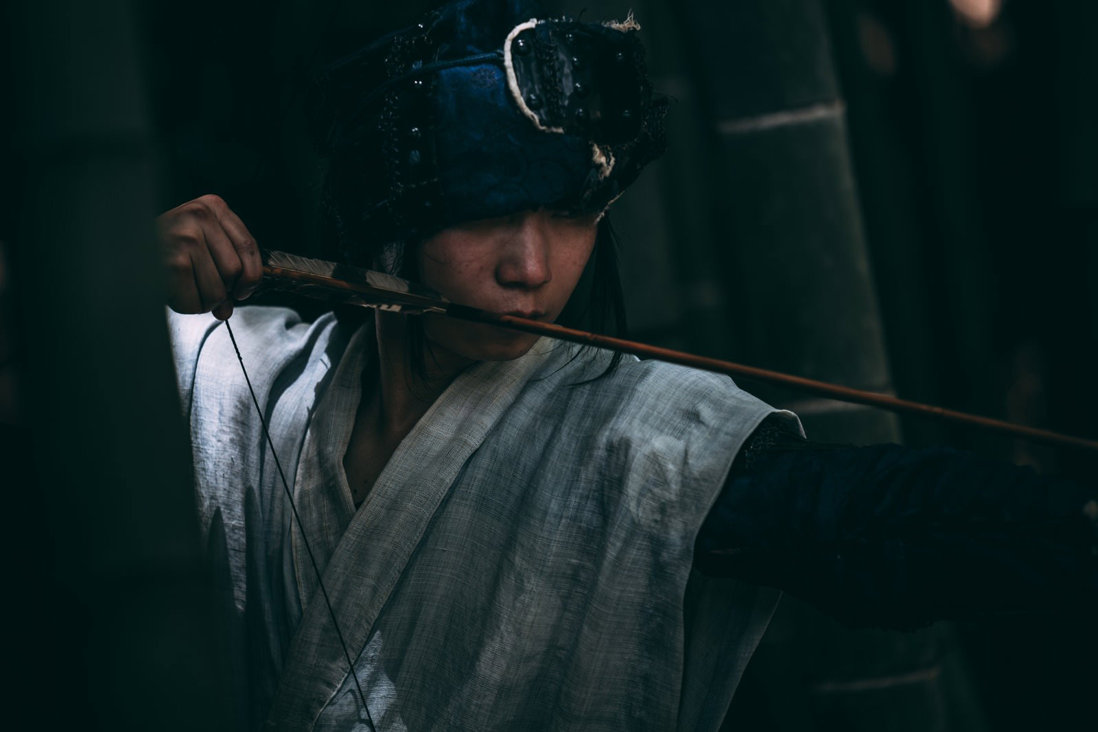 暗がりの中で弓矢を構える武装した野盗の男性［モデル：まーこ］