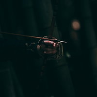 暗がりの中で握りしめる弓柄を持つ武装した男性の写真