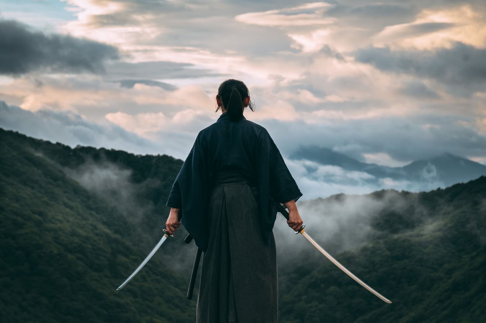 山頂で両手に刀を構える袴姿の武士が雲海を見下ろす［モデル：まーこ］