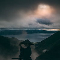 灰色の空の下、笠に手を添える侍のシルエットの写真