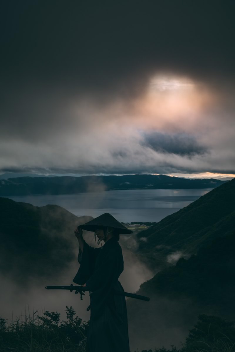灰色の空を背景に笠に手を添える侍のシルエット［モデル：まーこ］