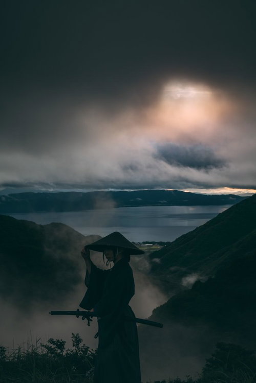 灰色の空の下、笠に手を添える侍のシルエット