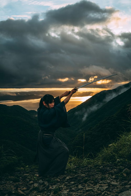 御霊櫃峠の夕景を背景に日本刀を切り上げる侍