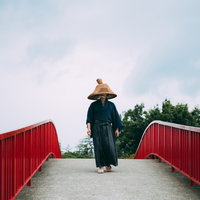 網代笠を被り赤い手すりの橋を渡る侍の後ろ姿の写真