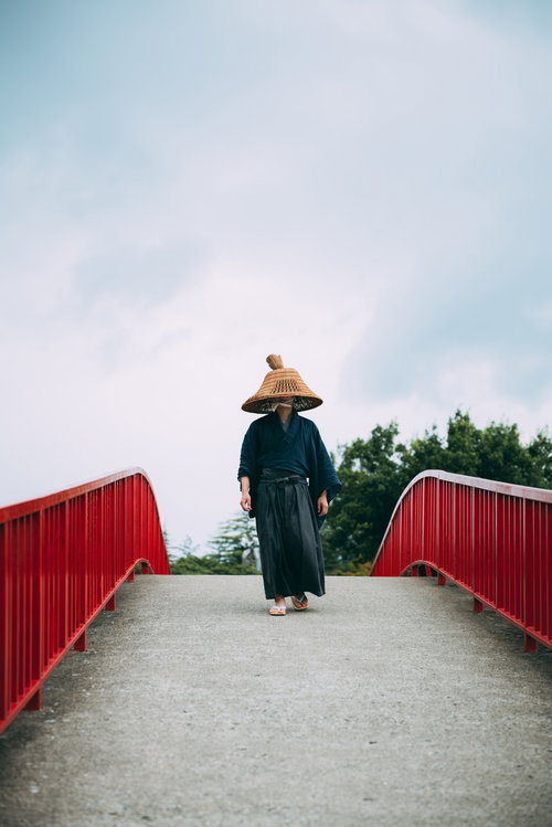 網代笠を被り赤い手すりの橋を渡る侍の後ろ姿