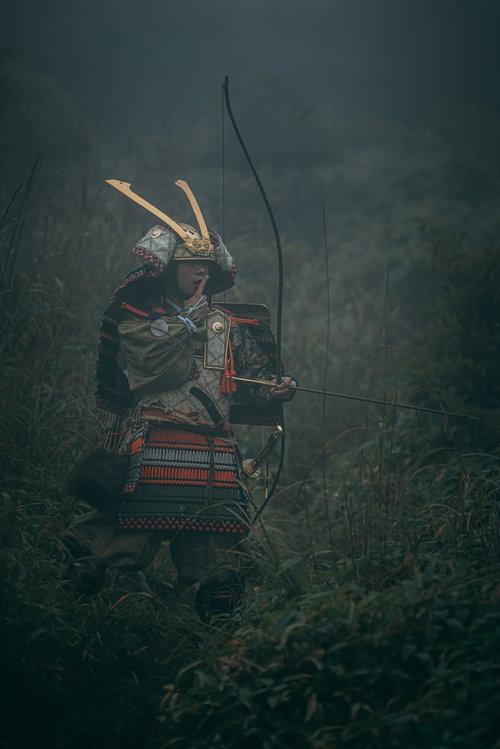 指を舐める大鎧を纏った侍のポーズ 森で弓を構える武士