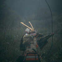 薮の中で大弓を引く侍の武士、鎧姿で矢を番えて狙うの写真