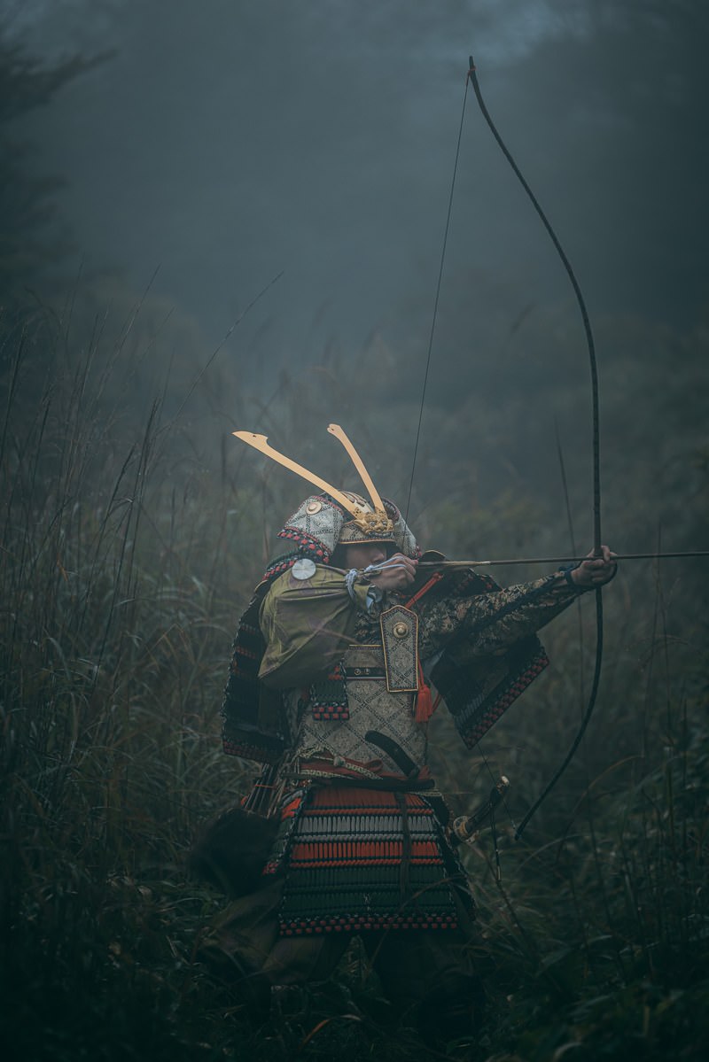薮の中で大弓を引く侍の男性が弓を構えている［モデル：まーこ］