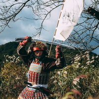 白い布を高く掲げて刀を頭上に構える当世具足姿の武士の写真