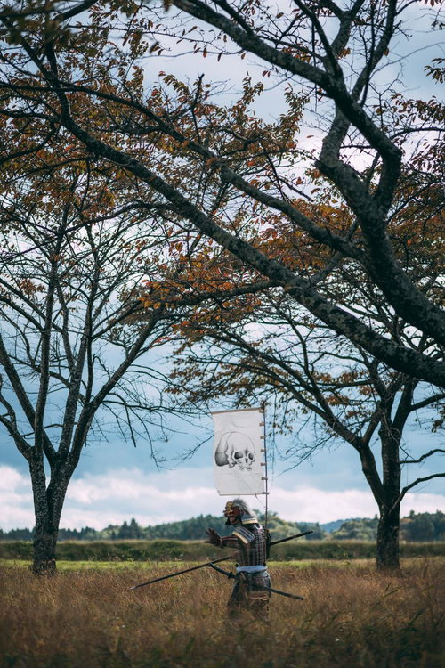 草原で棍棒を構える指物を立てた甲冑姿の武士