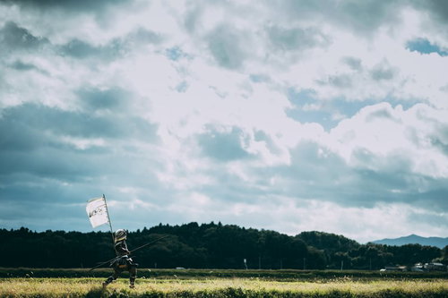 指物を風に揺らし棍棒を持ちながら逃走する侍