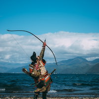 湖畔の山々を背景に空に向かって大弓を引く武士の写真