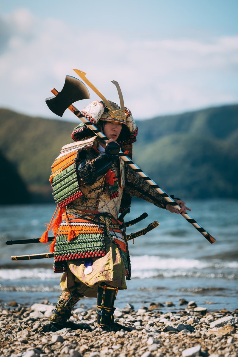 中州の河原で斧を担いだ大鎧姿の侍が歩いている［モデル：まーこ］