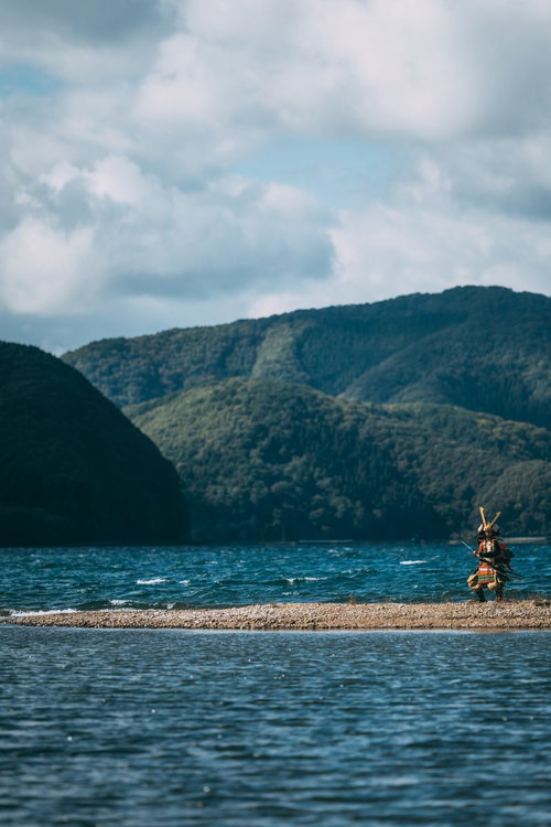 川の中州で刀を振り回す大鎧を身にまとった侍の戦闘シーン