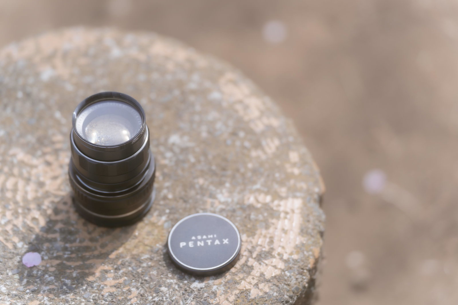 石の上に置かれたPENTAXのカメラレンズとレンズキャップを天日干ししている様子