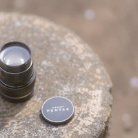 石の上で天日干しするPENTAXレンズとレンズキャップの写真