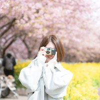 写ルンですで春の景色を撮影する白いジャケットの女性の写真