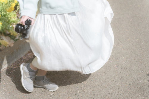 カメラを持ち、ひらめくスカートの裾を撮影する女性