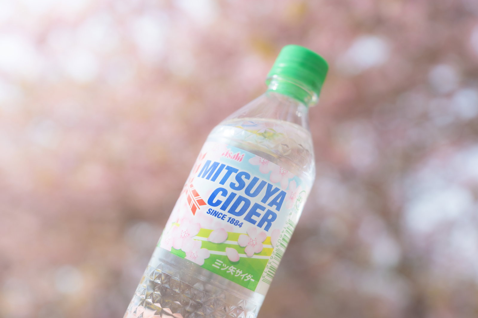 桜の前に構えた三ツ矢サイダーのボトル
