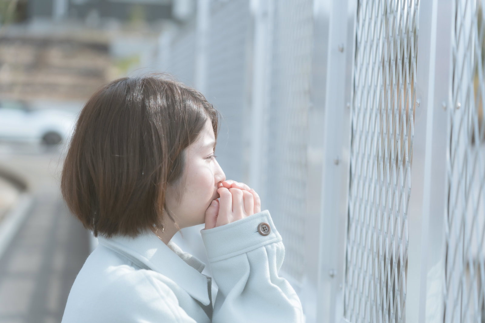 フェンス前で手を顔に当てて涙を流している白いシャツの女性の横顔