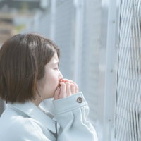 フェンス前で涙を流す白いシャツの女性の横顔の写真