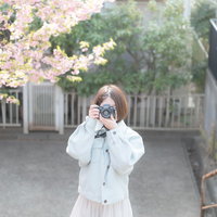 石段で桜を撮影するカメラを構える白いコートの女性の写真
