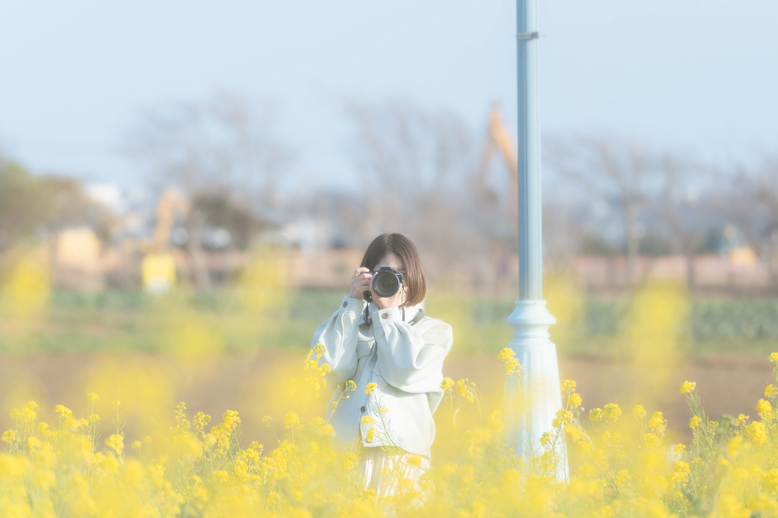 満開の菜の花畑でカメラを構えて撮影する女性フォトグラファー