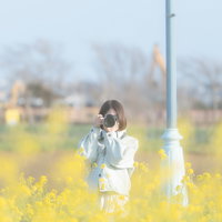 満開の菜の花畑でカメラを構える女性フォトグラファーの写真