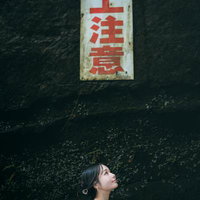 頭上注意の看板を見上げる女性と緑苔むした天井の写真