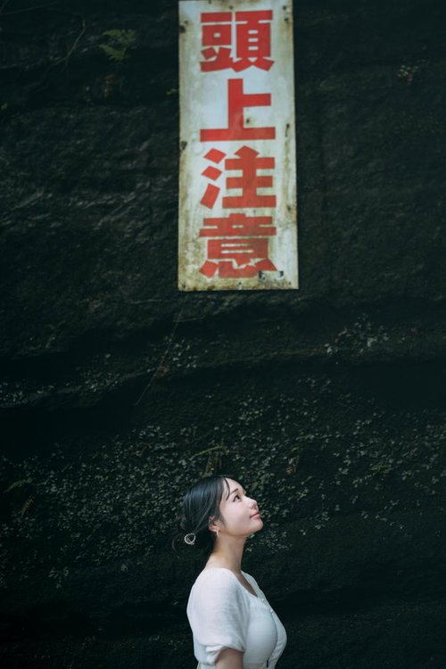 頭上注意の看板を見上げる女性と緑苔むした天井