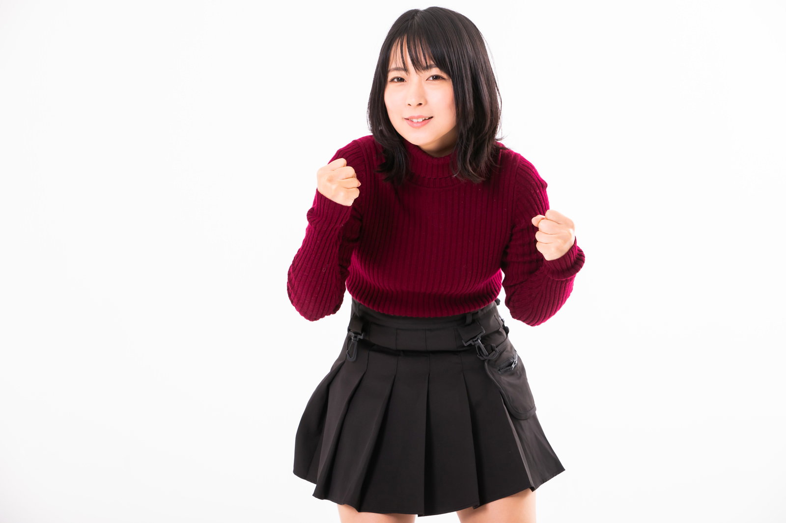 えんじ色のニットと黒いスカートを着た女性がガッツポーズをしている様子［モデル：にゃるる］