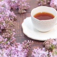 薄紫のライラックの蕾に囲まれたティーカップと紅茶の写真