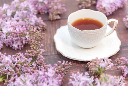 薄紫のライラックの蕾に囲まれたティーカップと紅茶