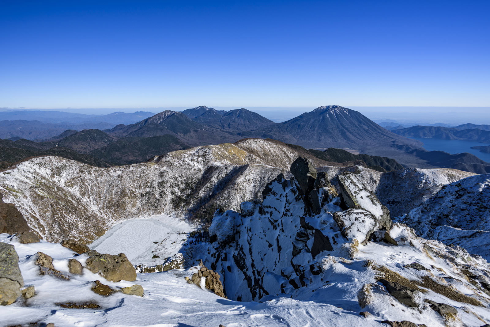 雪に覆われた日光白根山の山頂から見渡す青空と山々のパノラマ風景