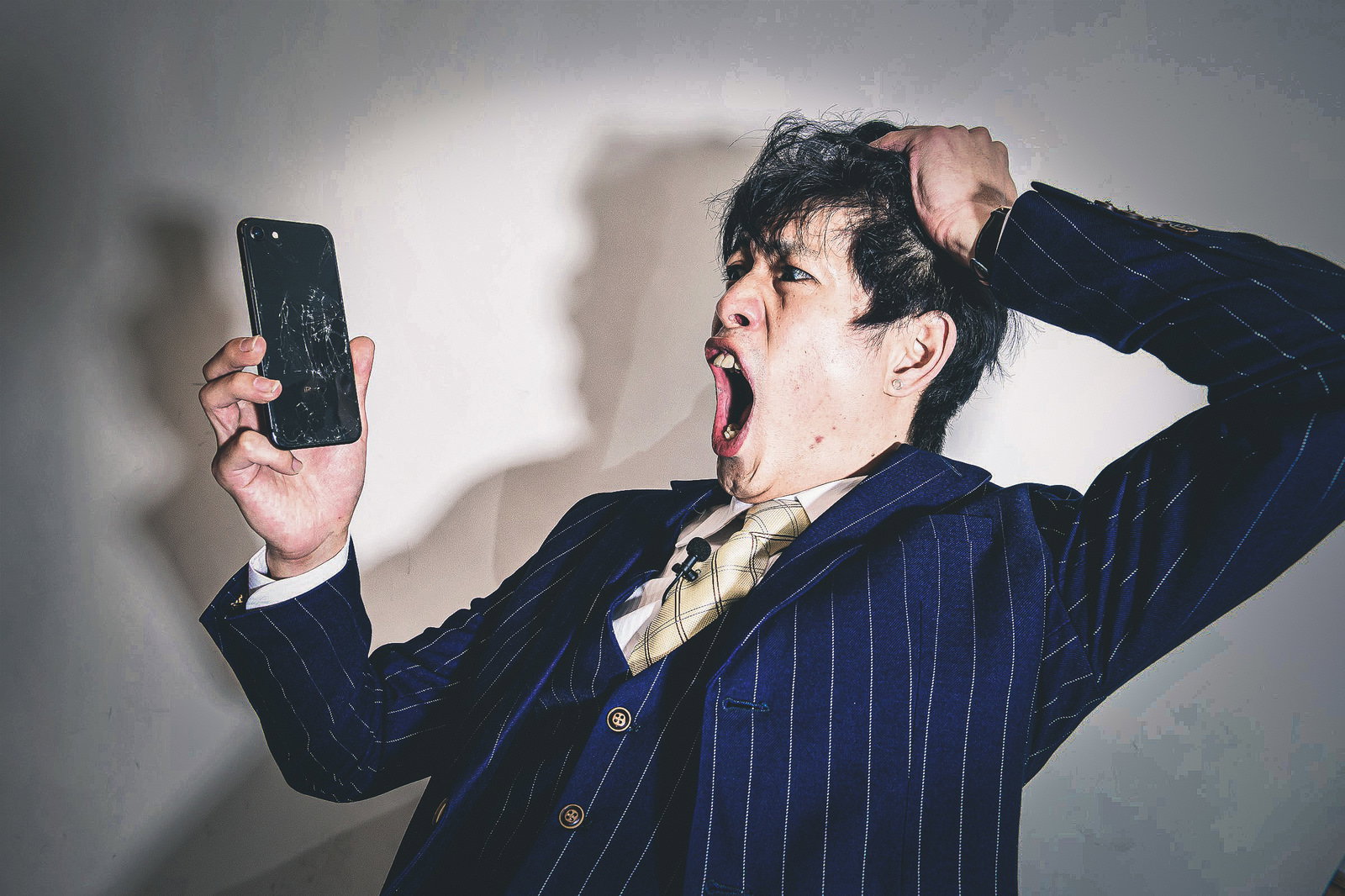 画面にヒビが入ったスマートフォンを持ちながら頭を抱えて困っている男性［モデル：モデルリリース］