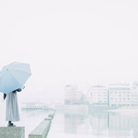雨の海辺で青い傘を差して歩く人物のシルエットの写真