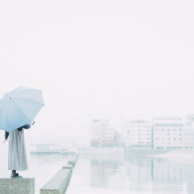 雨の海辺で青い傘を差して歩く人物のシルエットの写真