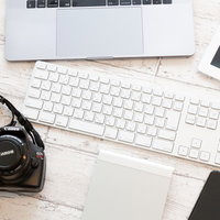 白いデスクに置かれたキーボードとミラーレスカメラの写真