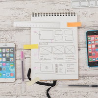 白いデスクに広げたスマホと手書きのデザインメモの写真